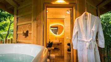 Een houten chalet met een jacuzzi, een houten bankje en een badjas hangend aan een rek.