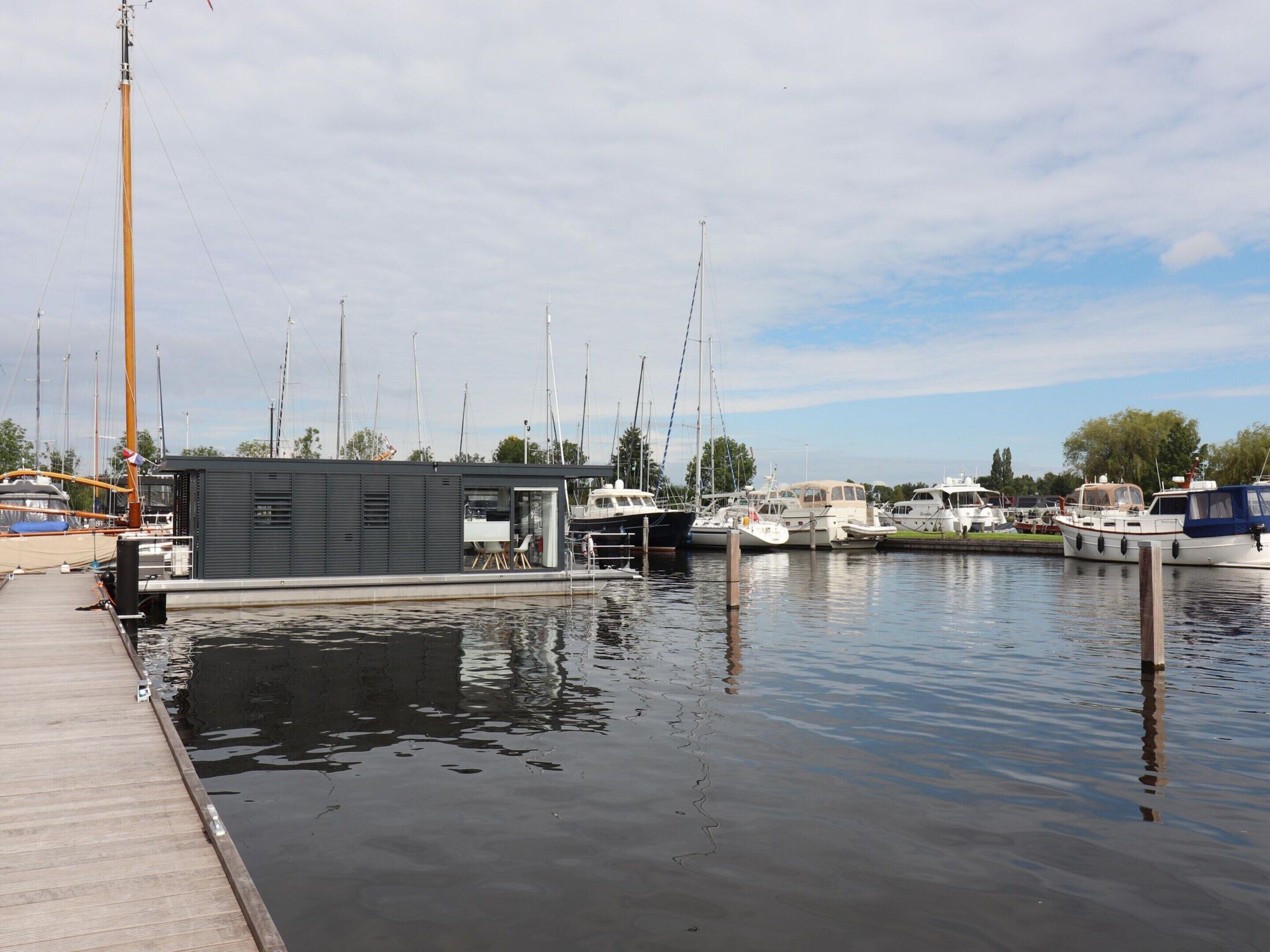 A marina with docked boats, a small building with a sloped roof, and calm water.