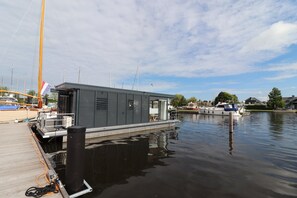 A docked boat with a small building, calm water, and a clear sky. - Houseboat in Lemmer With Harbor Views (Lemmer)