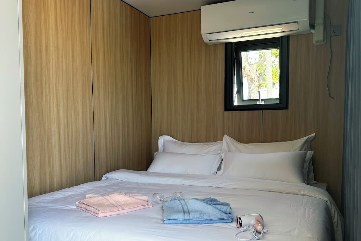 A bedroom with a bed, pillows, a window, and an air conditioning unit.