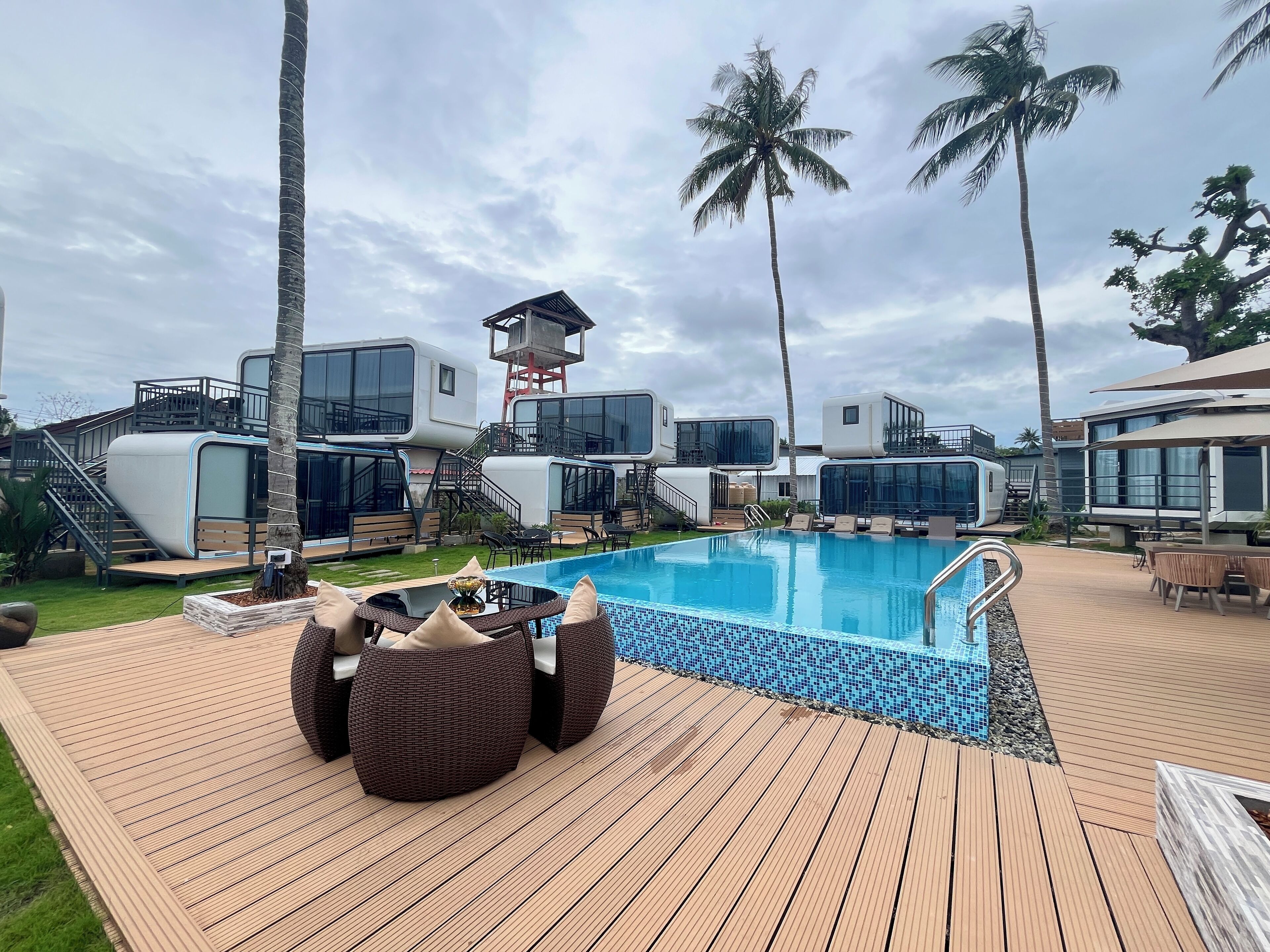 Uma área de piscina com villas modernas, uma torre salva-vidas e palmeiras.