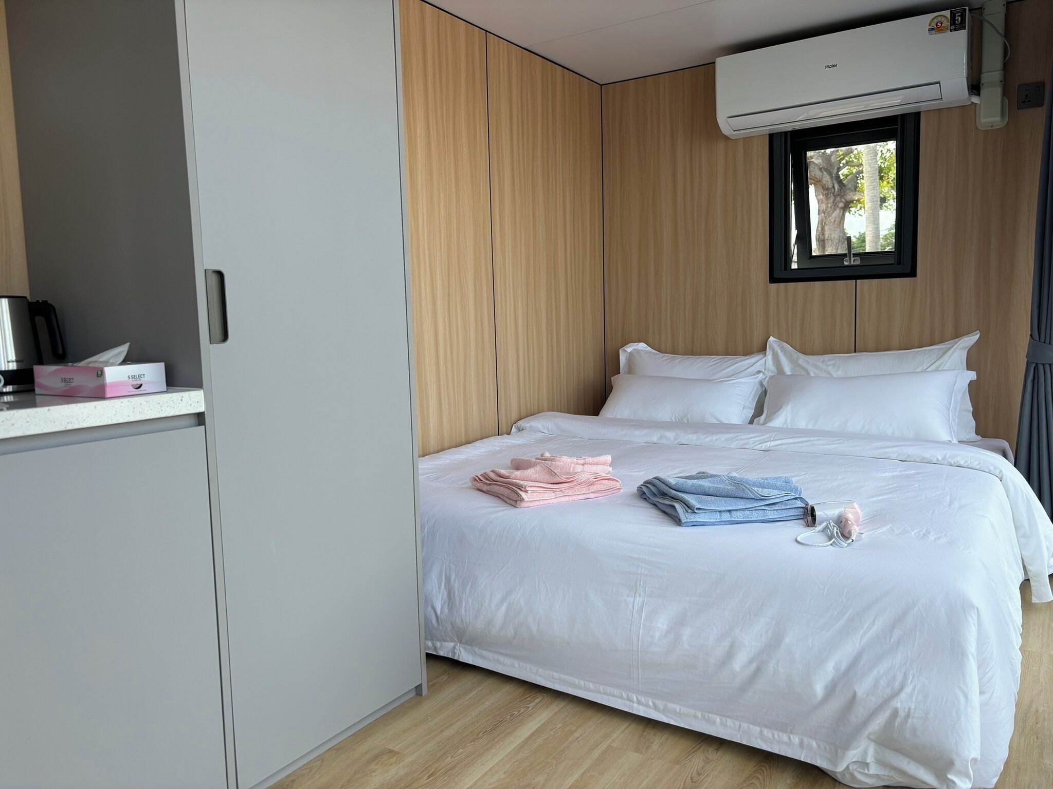 A hotel room with a bed, a small desk, and an air conditioning unit.