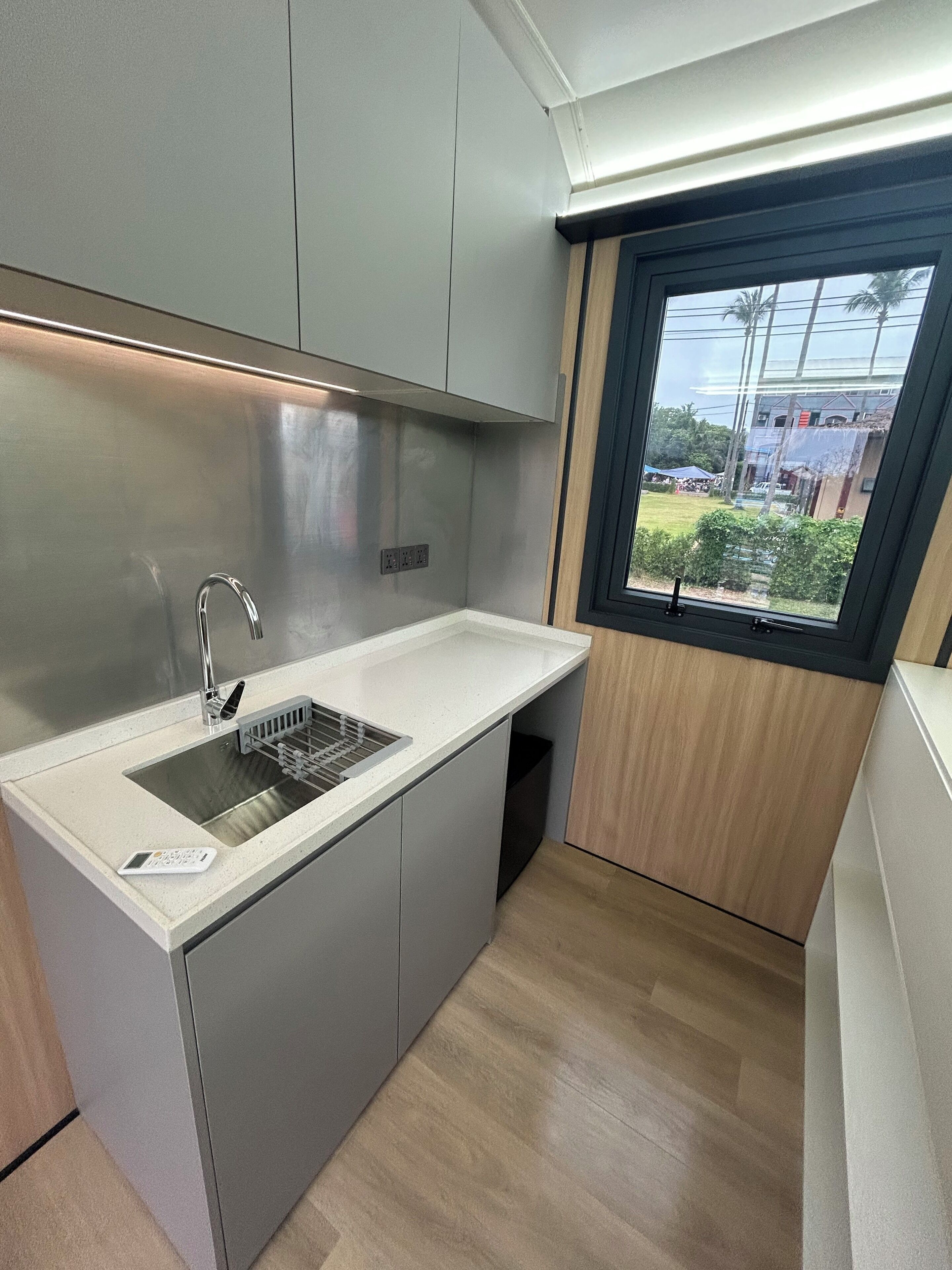 A compact kitchen with a stainless steel sink, a window with a view of the outside, and light-colored cabinetry.