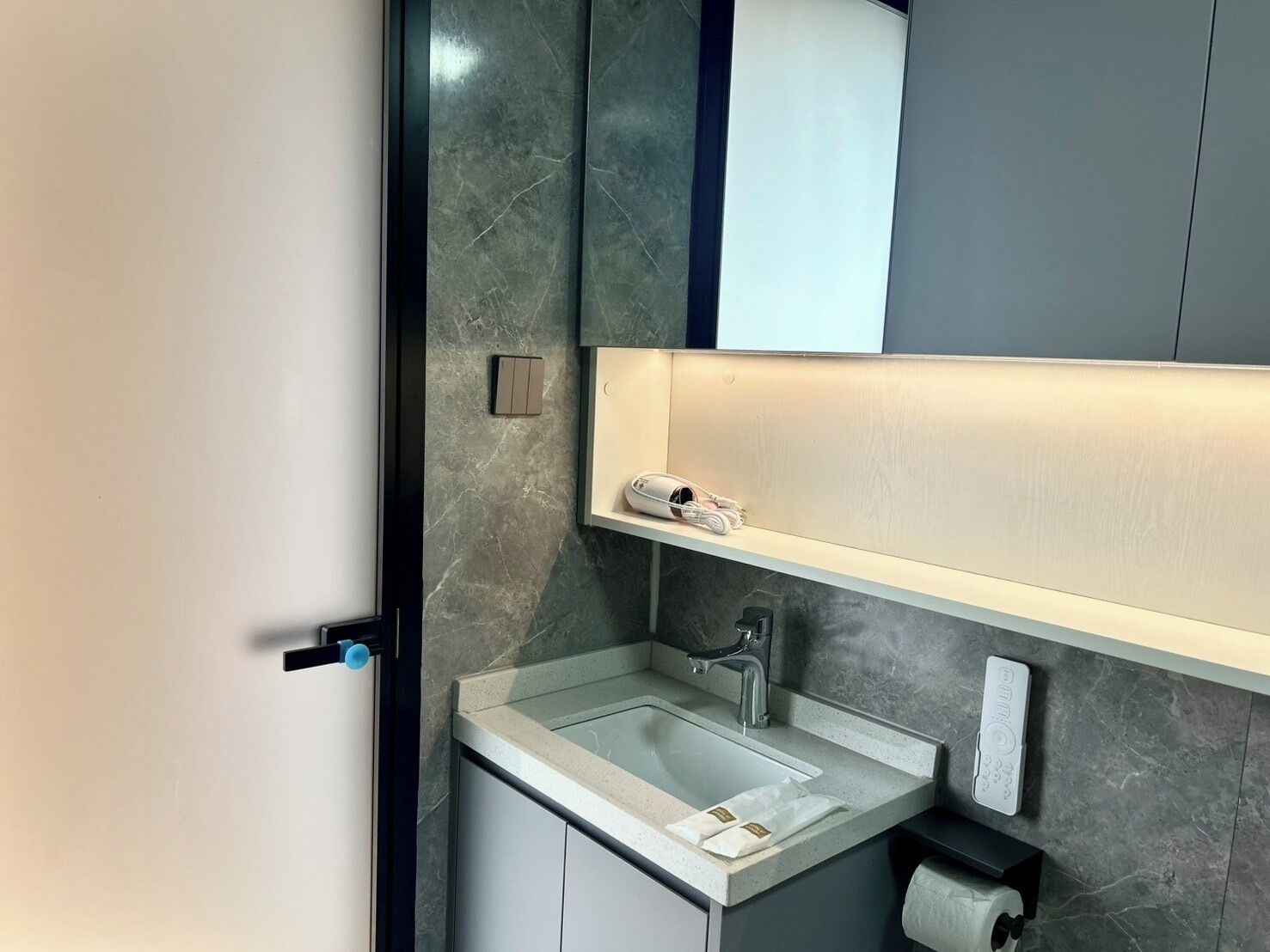 A modern bathroom with a marble sink, a mirror, a towel dispenser, and a toilet paper holder.