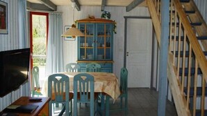 Un coin repas avec une table et des chaises, un meuble avec des portes en verre, un téléviseur et un escalier en bois.