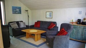 Un salon comprenant un canapé, un fauteuil et une table basse. On y trouve également un meuble et une lampe.
