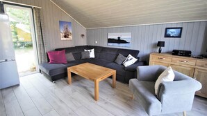 A modern living room with a sectional sofa, a wooden coffee table, a grey armchair, and a TV on a wooden cabinet. - Skandinavisches Ferienhaus in Mirow (Mirow)