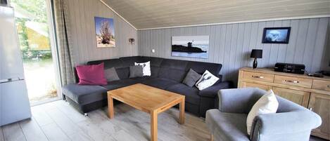 Una sala moderna con un sofá seccional, una mesa de centro de madera, un sillón gris y un televisor sobre un mueble de madera.