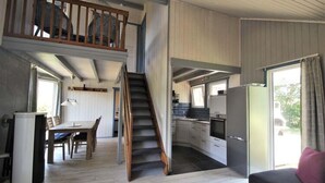 A spacious living area with a staircase leading to an upper level, a kitchen with modern appliances, and a dining area with a table and chairs. - Skandinavisches Ferienhaus in Mirow (Mirow)