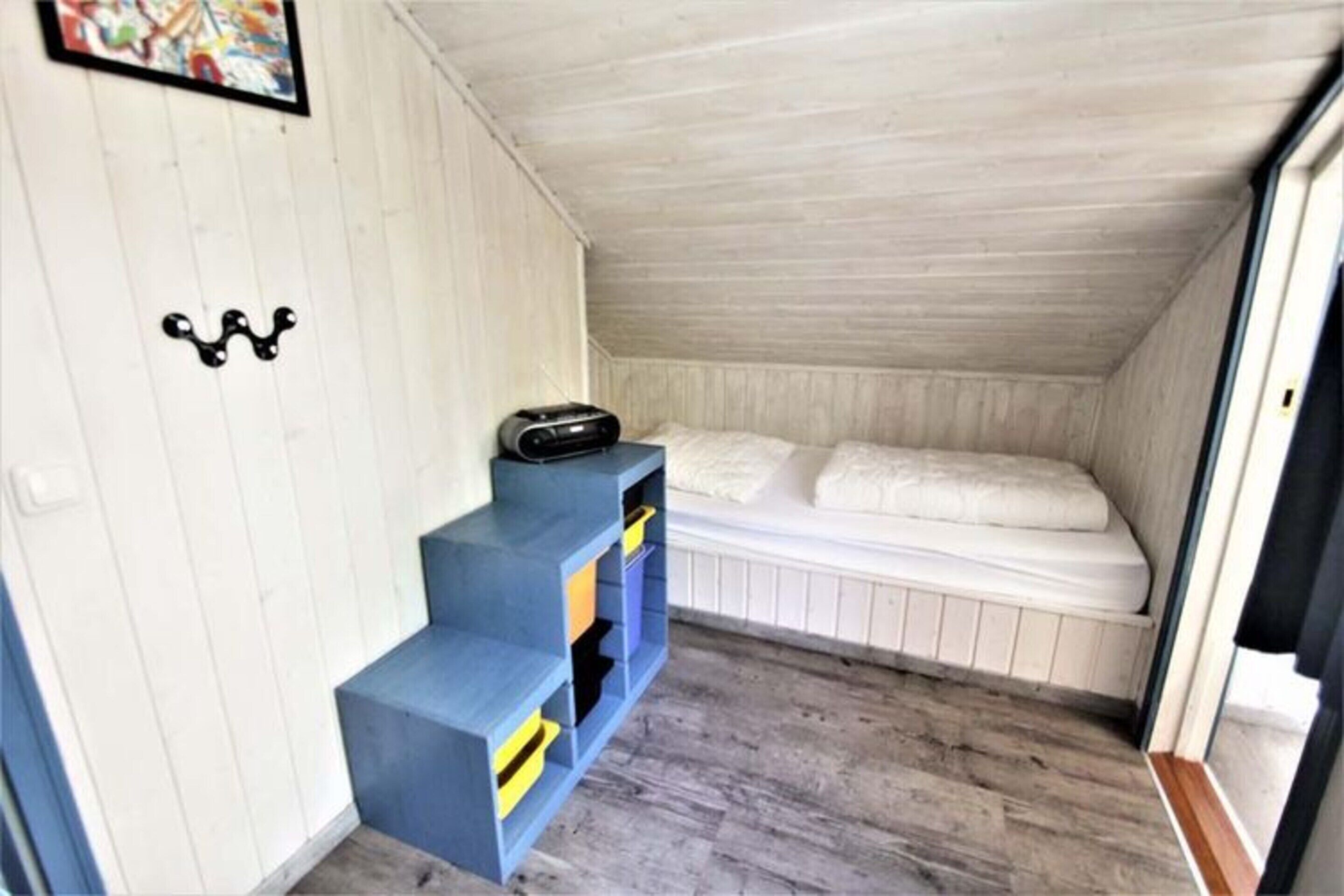 Ein kleines Schlafzimmer im Dachgeschoss mit Etagenbett, blauem Stauraum mit Schubladen und Holzboden.