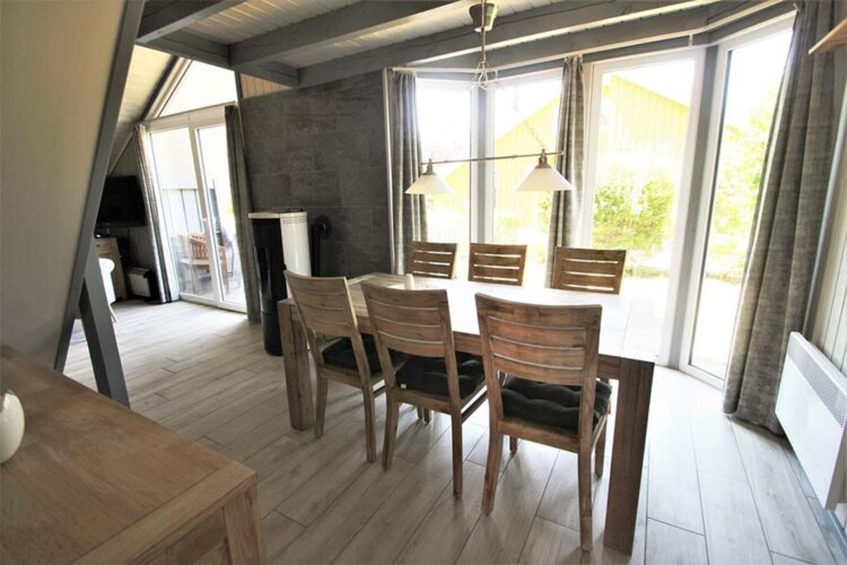 A dining area with a wooden table and chairs, large windows with curtains, and a ceiling fan.