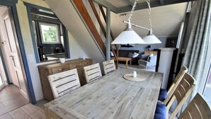 A dining area with a wooden table and chairs, a hanging light fixture, and a view of the kitchen and living area. - Skandinavisches Ferienhaus in Mirow (Mirow)