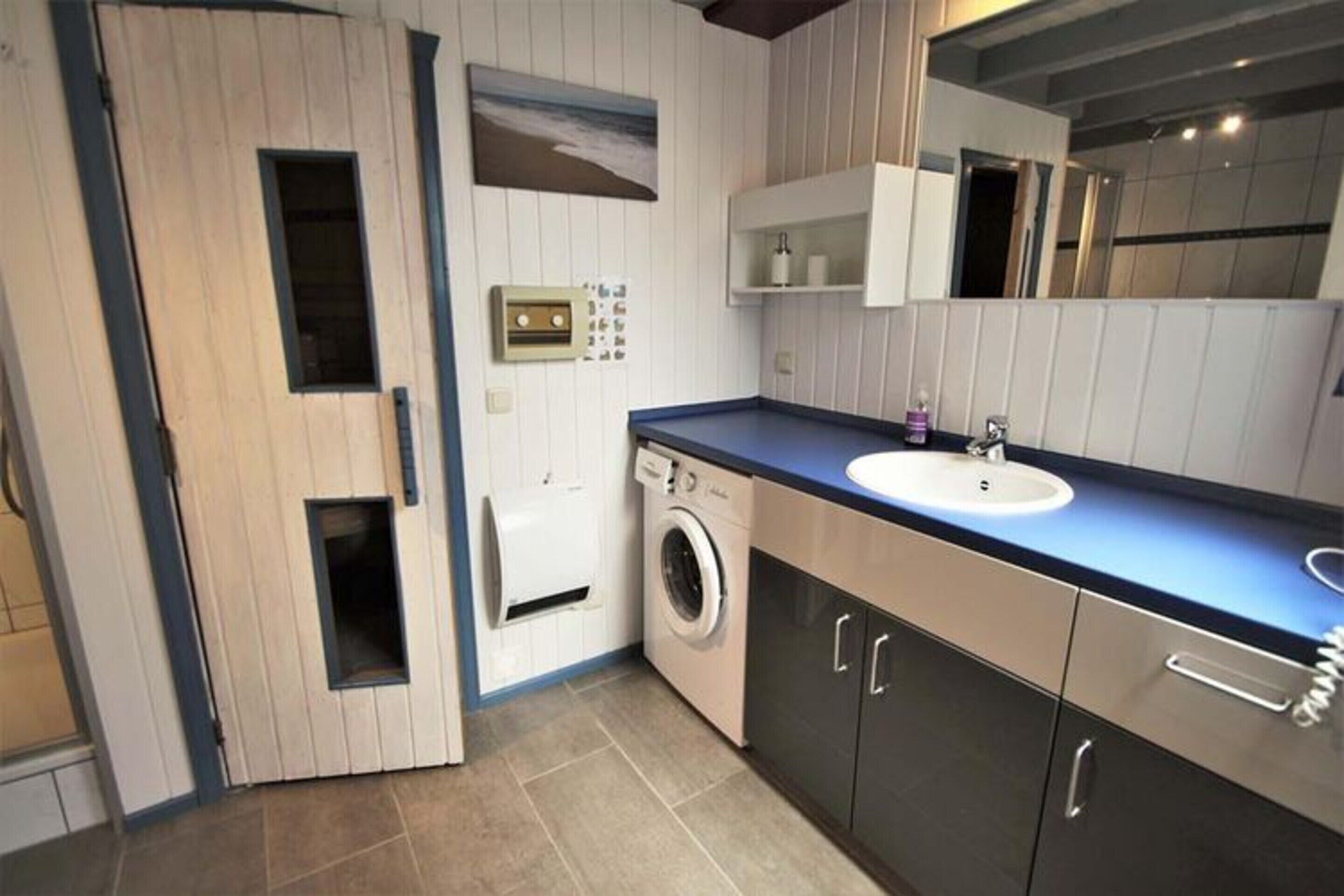 A compact bathroom with a washing machine, a sink, and a mirror.