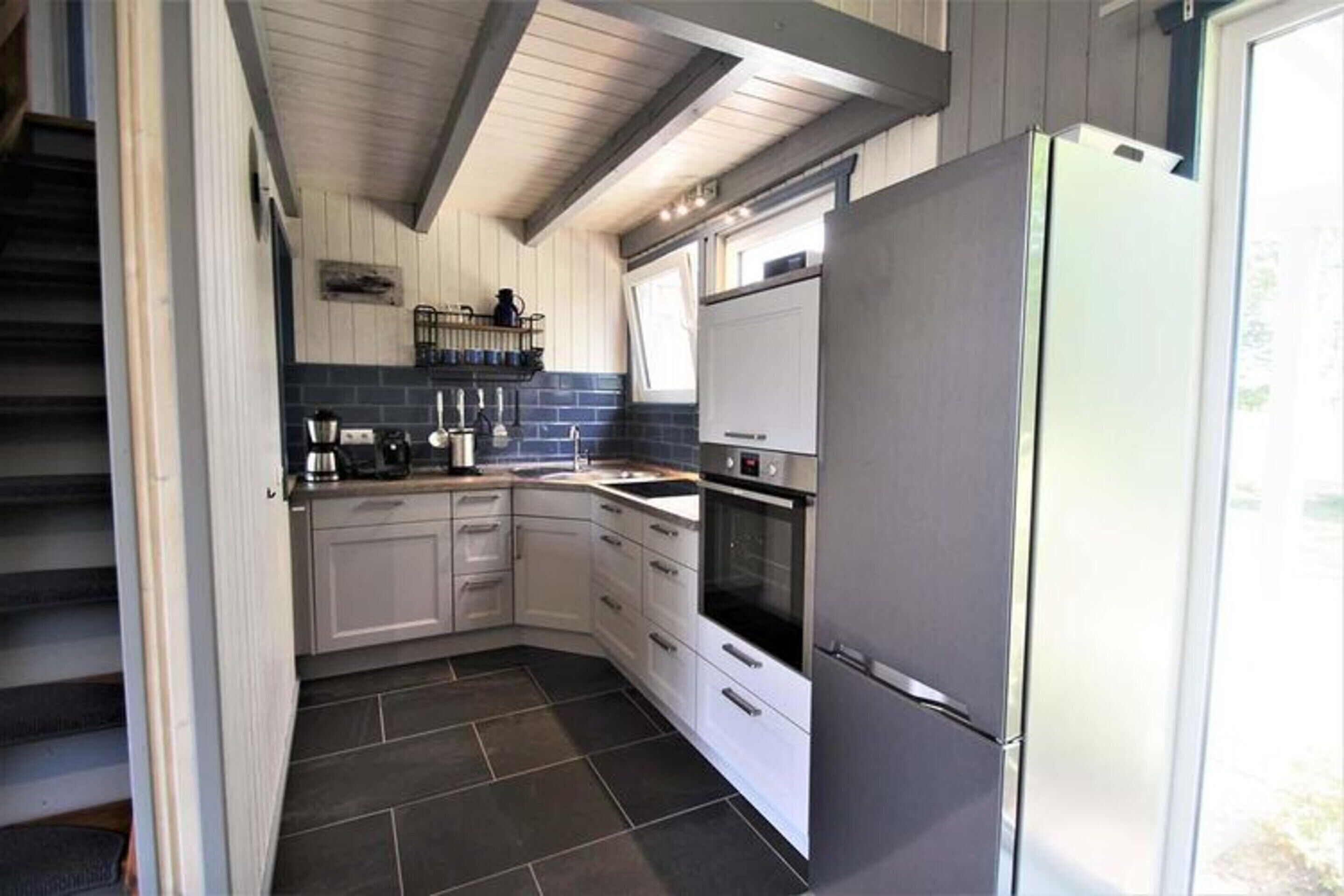 A compact kitchen with white cabinets, a stainless steel refrigerator, and a built-in oven.