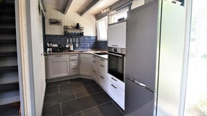 A compact kitchen with white cabinets, a stainless steel refrigerator, and a built-in oven. - Skandinavisches Ferienhaus in Mirow (Mirow)