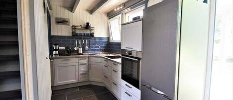 Una cocina compacta con armarios blancos, un refrigerador de acero inoxidable y un horno empotrado.