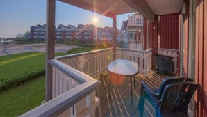 Un balcon avec une table et des chaises, donnant sur un quartier résidentiel avec des maisons et un ciel dégagé.