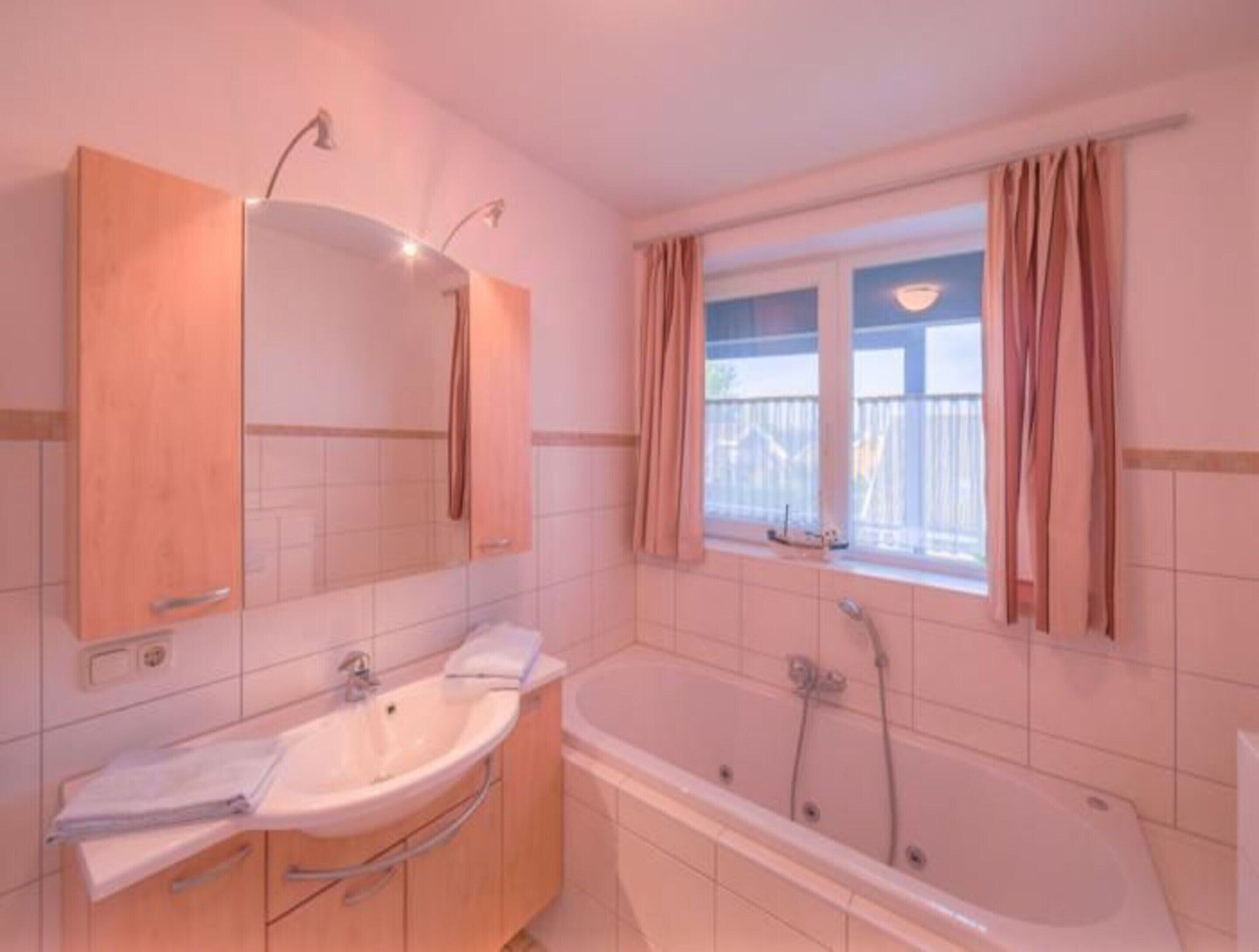 A bathroom with a bathtub, a sink, and a window with curtains.