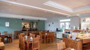A spacious dining area with wooden tables and chairs, a kitchen in the background, and a bar area with a counter and stools.