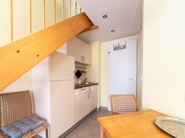 A compact kitchen with a wooden staircase, a dining table, and a wicker chair.