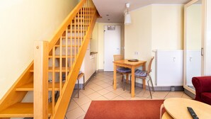 A room with a wooden staircase, a dining table with chairs, a red sofa, and a TV. - Elegant Eingerichtete Ferienwohnung (Mirow)