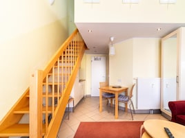 A room with a wooden staircase, a dining table with chairs, a red sofa, and a TV.