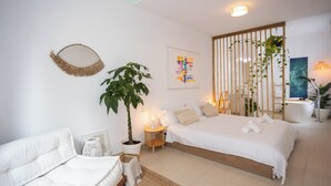 A modern bedroom with a large bed, a sofa, a potted plant, and a wall-mounted artwork. - Villa Naim Guest House Cala del Moral (Rincon de la Victoria)