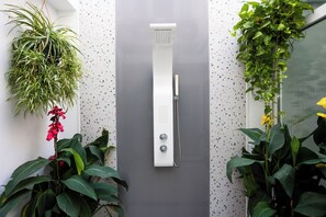 Een moderne douche met bedieningspaneel, omgeven door groene planten.