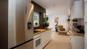 A modern kitchen with stainless steel appliances, a wooden countertop, and a built-in oven. There is a window with a view of greenery outside, and a chair is placed near the window. - Villa Naim Guest House Cala del Moral (Rincon de la Victoria)