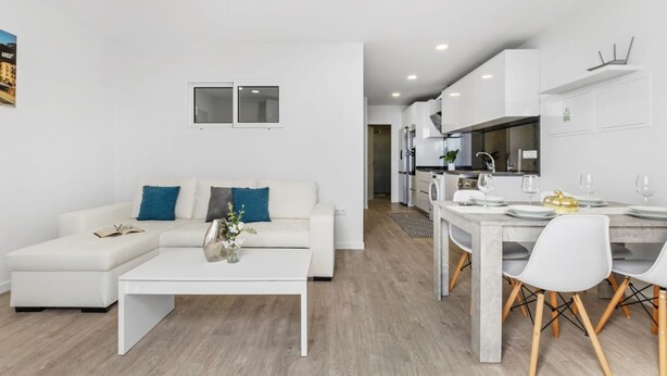 A modern living room with a white sofa, a coffee table, and a dining area with a table set for four.