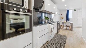 A modern kitchen with a built-in oven, microwave, and washing machine. There is a dining area with a table and chairs.