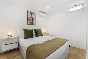 A neatly arranged bedroom with a bed, green pillows, a bedside lamp, and a wall-mounted air conditioner. - Serene Blue Escape by Madeira Sun Travel (Ponta do Sol)