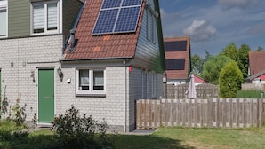 Una casa de dos pisos con techo inclinado, paneles solares, una puerta verde y fachada de ladrillo.