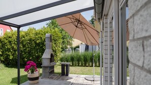 Un patio al aire libre con una parrilla de piedra, una mesa con una cesta tejida y una sombrilla grande que proporciona sombra.