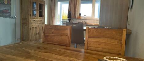 Een kleine keuken met houten kastjes, een eettafel en uitzicht op de omgeving door een raam.
