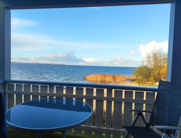 A balcony with a table and chairs, overlooking a body of water and a grassy area. - Appartement im Ferienpark in Rechlin (Rechlin)