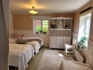 Une chambre avec deux lits, une commode blanche, une fenêtre donnant sur un paysage verdoyant et un luminaire au plafond.