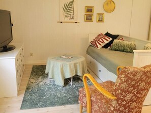 Quarto pequeno e acolhedor, com uma cama, uma cadeira, uma mesa e uma televisão.
