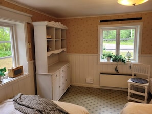A room with a bed, a white cabinet with shelves, a chair, and a window with a view of greenery. - 6 Person Holiday Home in Bergsjo (Bergsjo)