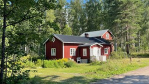 A red wooden cabin with a metal roof, surrounded by dense forest and a gravel path. - 6 Person Holiday Home in Bergsjo (Bergsjo)