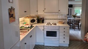 A compact kitchen with white cabinets, a stove, and a microwave. There is a dining area visible in the background.