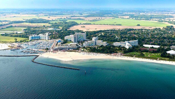 Vista aérea de un complejo turístico costero con varios edificios de gran altura, un puerto deportivo y una playa.