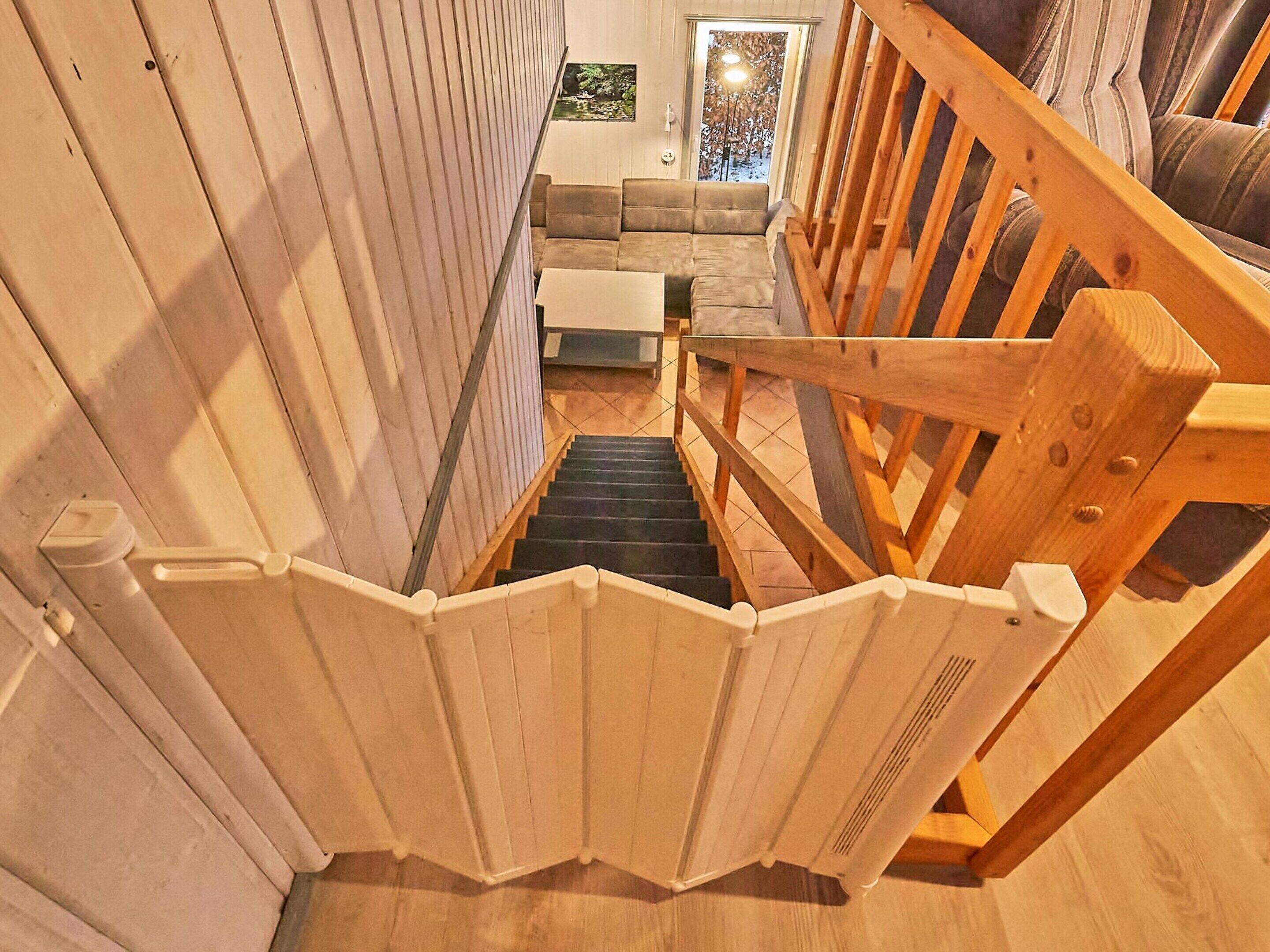 A wooden staircase with a handrail leading to a living area with a sofa and a view of the outdoors.