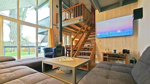 Un salon spacieux avec un grand canapé, un escalier en bois et un téléviseur fixé au mur.