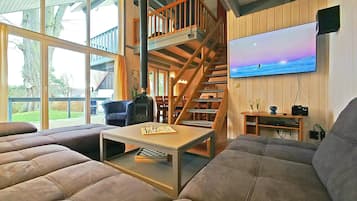 Amplia sala de estar con un sofá grande, una escalera de madera y un televisor montado en la pared.