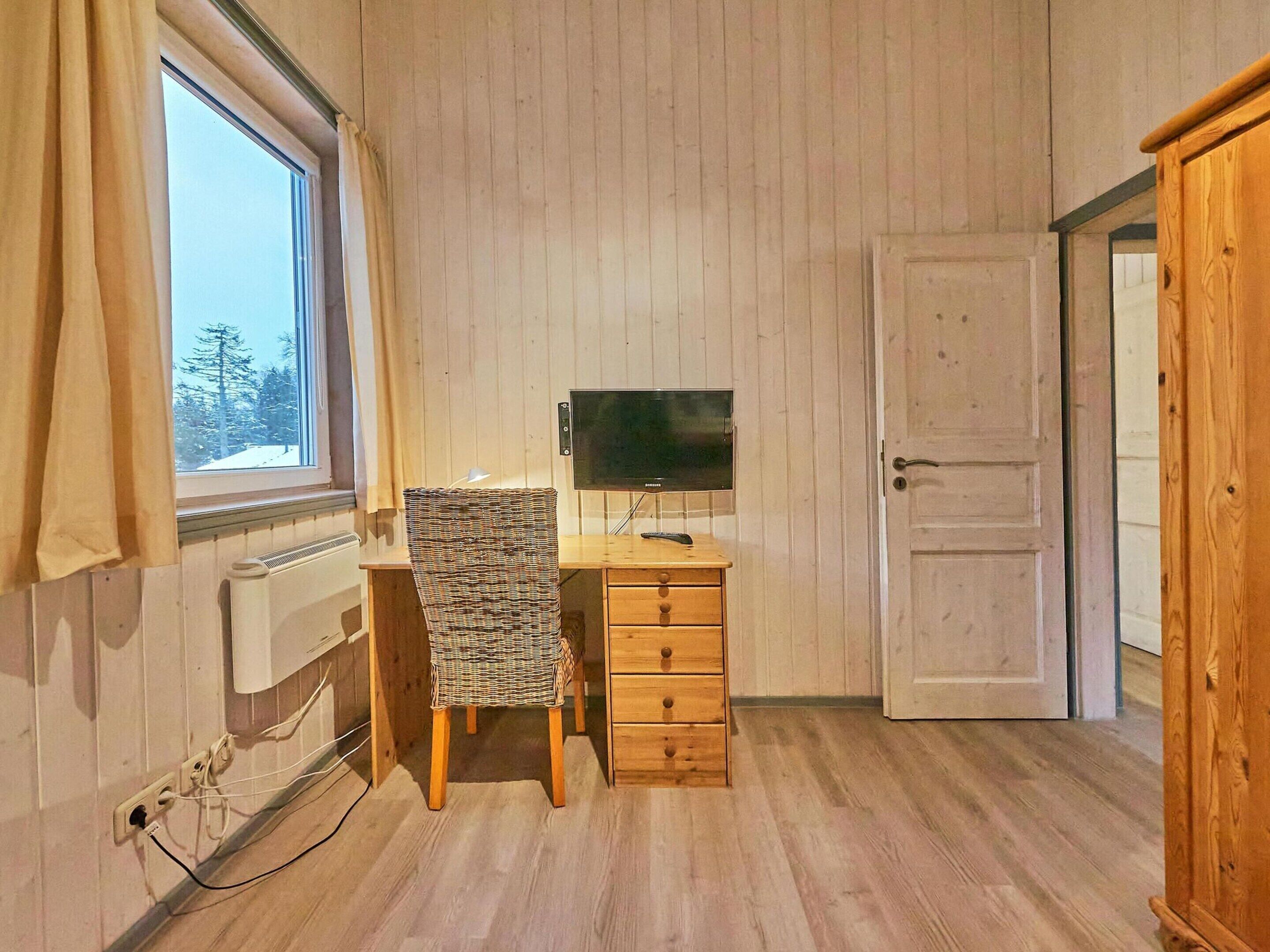 Una habitación con un escritorio de madera, una silla, un televisor y una puerta.