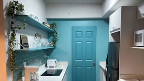 Een kleine keuken met een blauwgroene deur, witte aanrechtbladen en een ingebouwde magnetron.