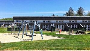 Un terrain de jeux avec des balançoires et un bac à sable, situé devant un bâtiment doté de nombreuses fenêtres et d’une façade en briques.