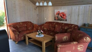 Una habitación acogedora con techo de madera, un sofá rojo con estampado, una mesa de centro de madera con un jarrón de flores y un cuadro de flores rojas en la pared.