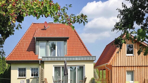 A two-story house with a red-tiled roof, a balcony with outdoor furniture, and a garden with rocks and plants. - Ferienhaus, Fedderwardersiel (Butjadingen)